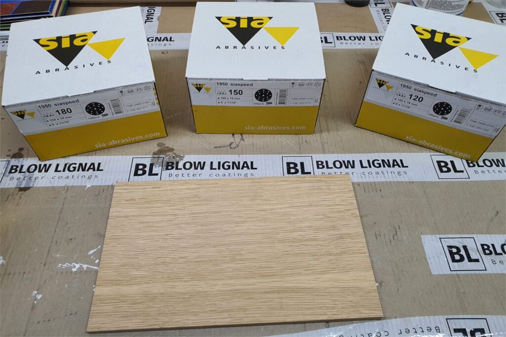 Przygotowanie forniru dębowego do olejowania: surowa powierzchnia drewna i papiery ścierne Sia Abrasives do szlifowania wstępnego.